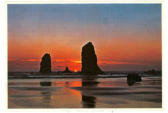 The vivid glow of sunset-tinted clouds silhouette The Needles on Cannon Beach, OR - Carey's Emporium